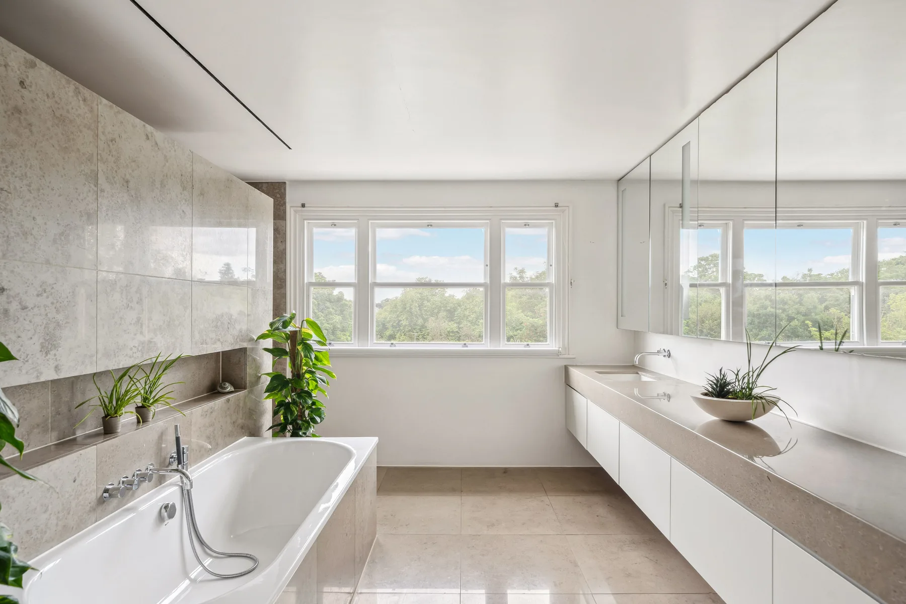 Un baño luminoso con bañera, un lavabo largo y ventanas amplias.
