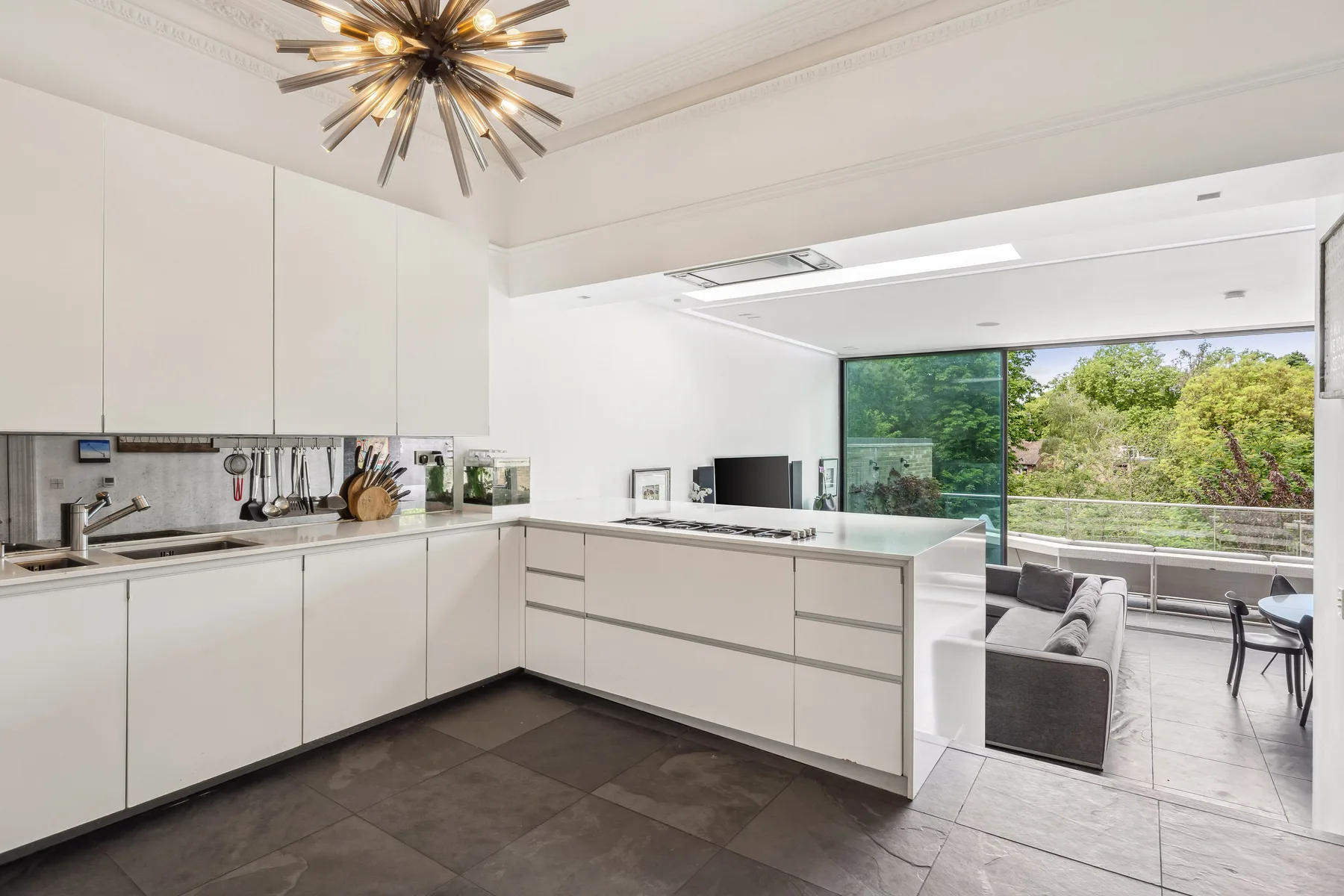 A bright modern kitchen opens onto a living area with large windows.