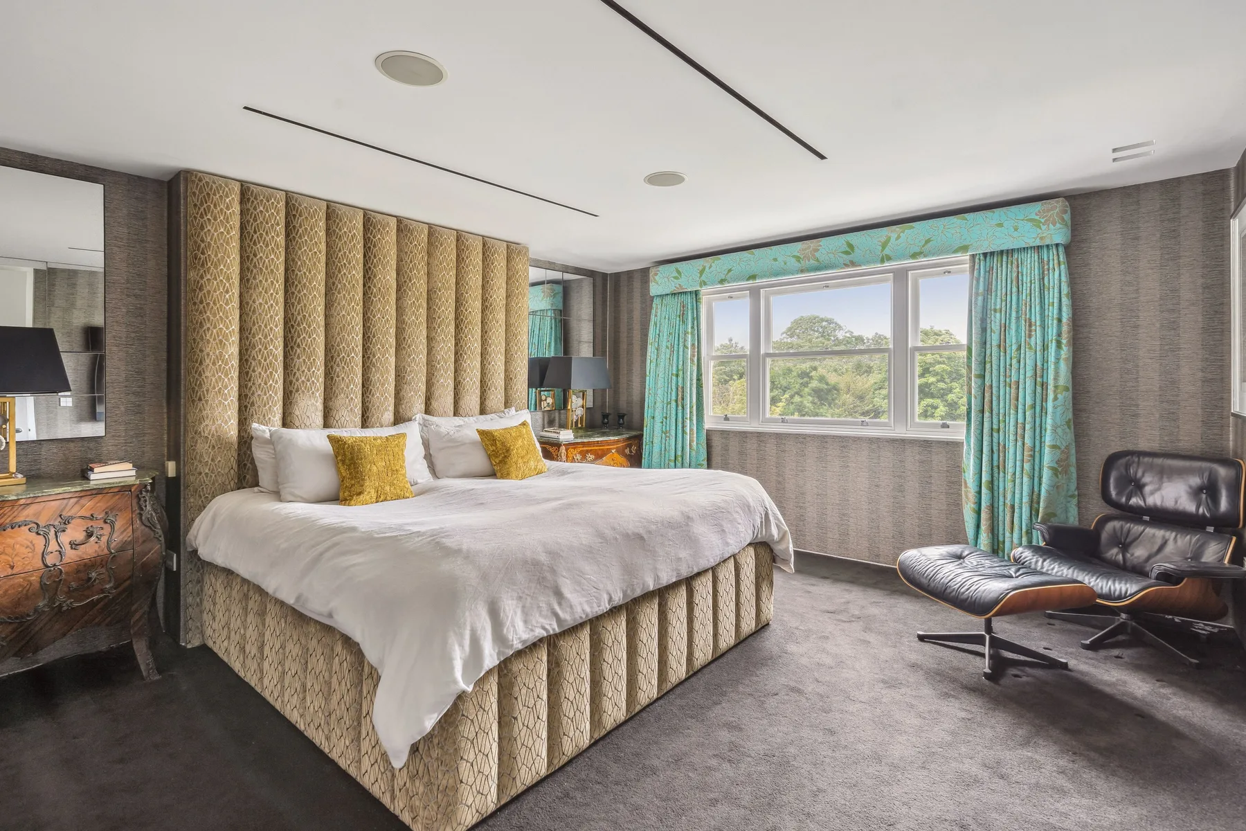 Un dormitorio con una cama grande, un cabecero estampado y ventanas junto a un sillón.