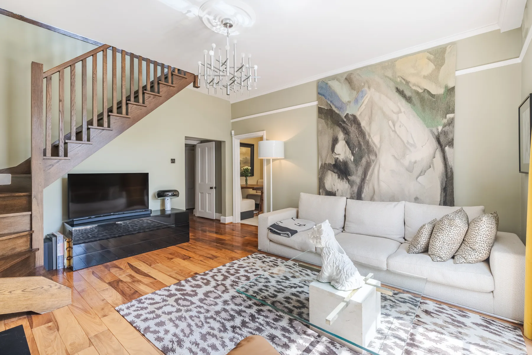 Una sala luminosa con sofá blanco, alfombra estampada y escalera.