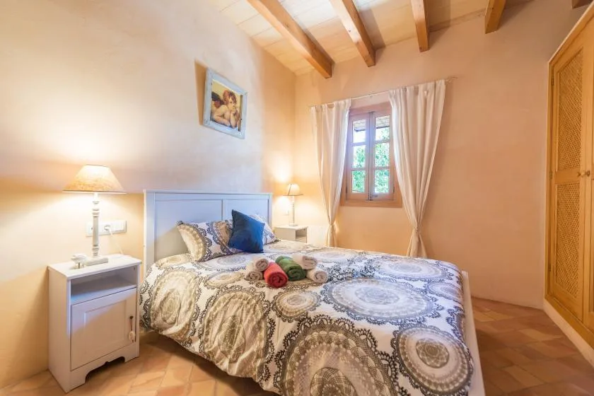 A bedroom with a patterned bedspread and a window framed by curtains.