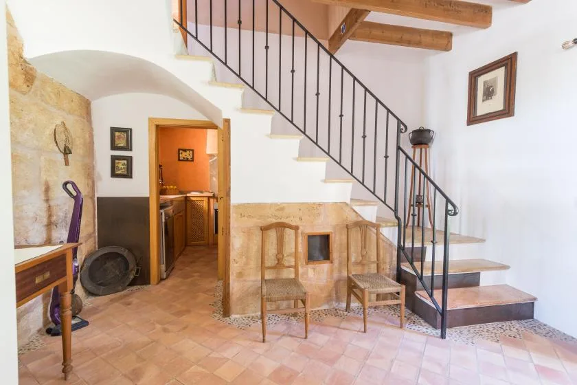 A tiled room with a staircase, wooden chairs, and an open doorway.