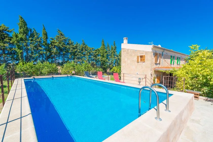 An outdoor swimming pool sits beside a stone house, with trees in the background.