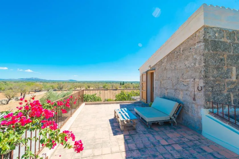 A sunlit outdoor terrace with lounge seating overlooks open countryside.