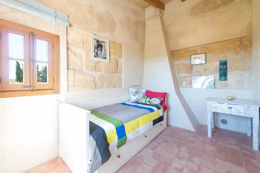 A bedroom with a single bed beside a wooden-framed window.