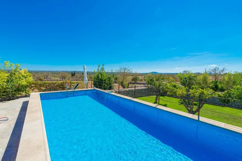 An outdoor swimming pool overlooks a green landscape beneath a clear blue sky.