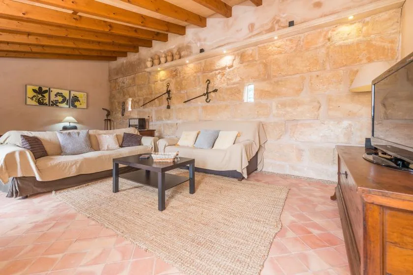 A living room with sofas around a coffee table beneath exposed wooden ceiling beams.