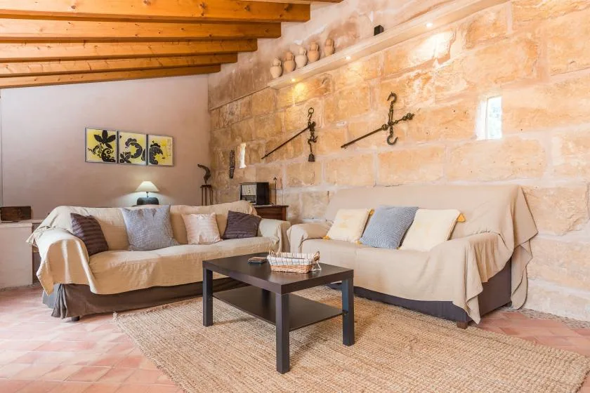 A living room with cushioned seating, a coffee table, and exposed wooden ceiling beams.