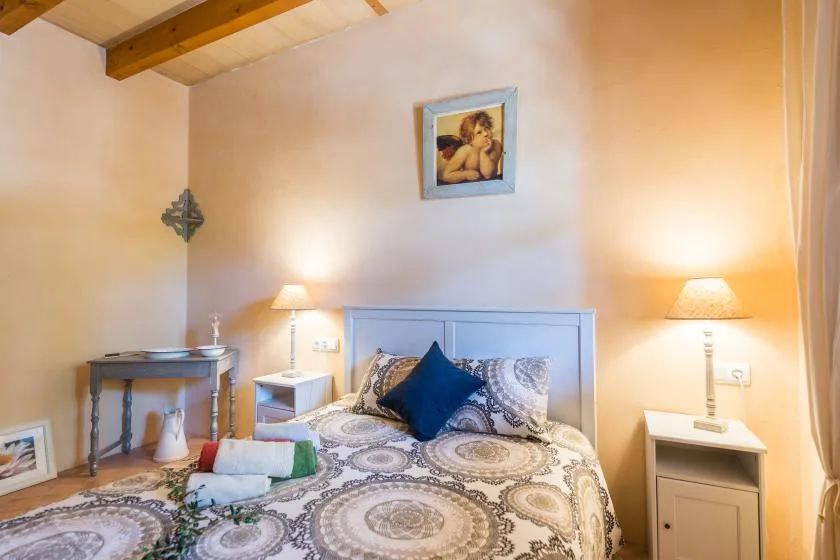 A warmly lit bedroom with patterned bedding and a framed picture above the bed.