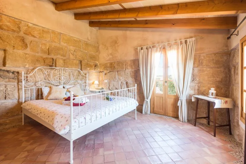 A bedroom with a white bed beside a curtained glass door.