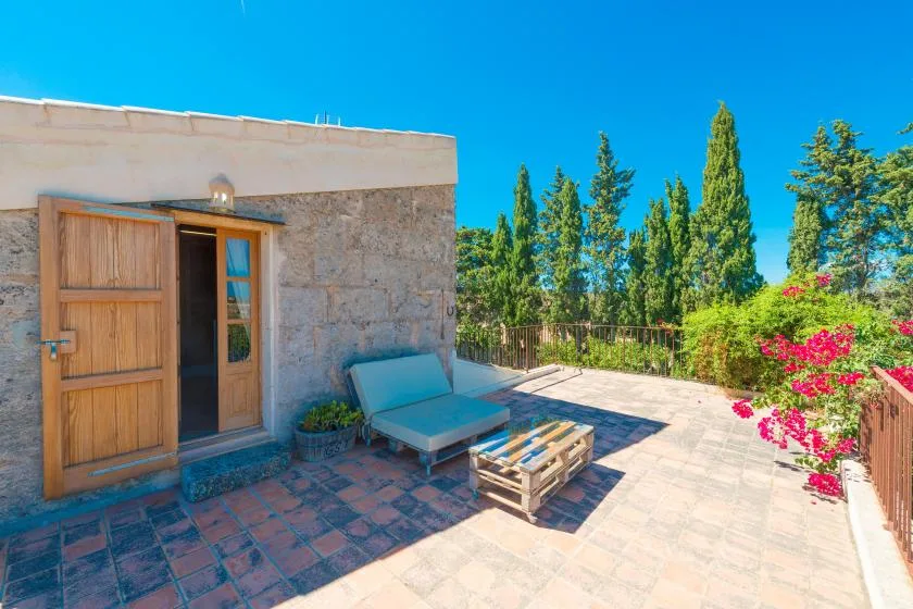 A sunny stone patio with outdoor seating and flowering plants.