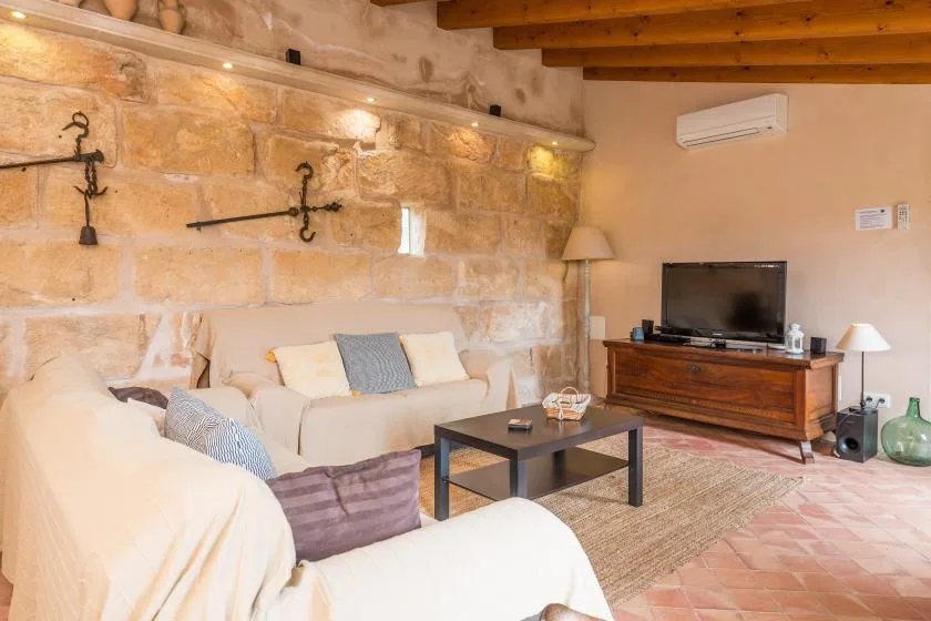 A living room with cream seating, a television, and exposed stone walls.
