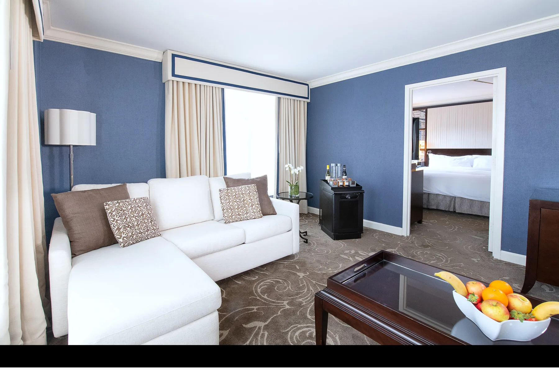 Sala de estar de la suite con sofá modular y dormitorio independiente con cama king