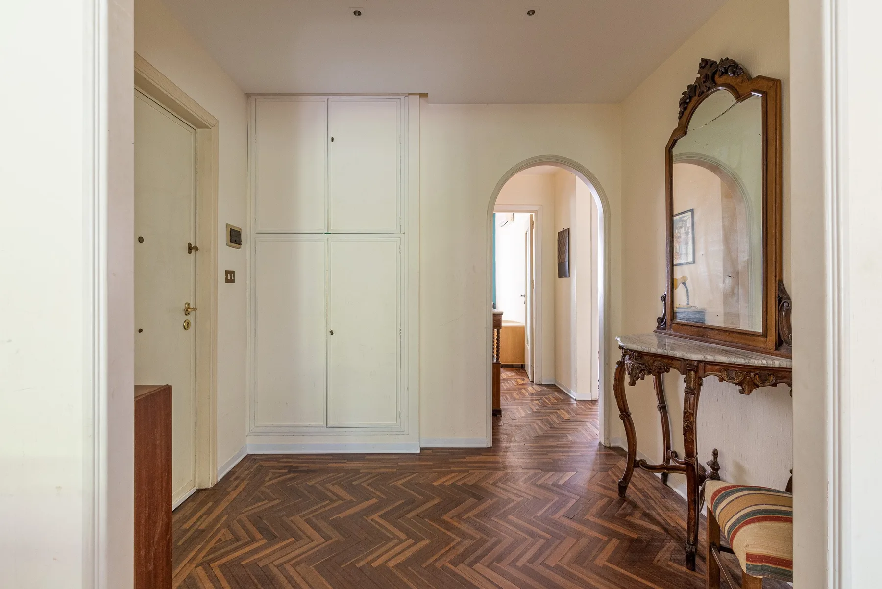 Un pasillo interior con suelo de parquet y una puerta arqueada.
