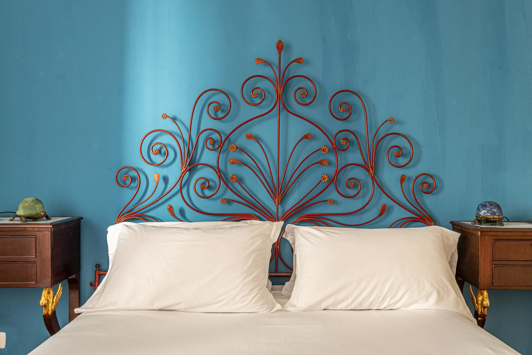 Un dormitorio con una cama frente a una pared azul decorada con metal ornamentado.