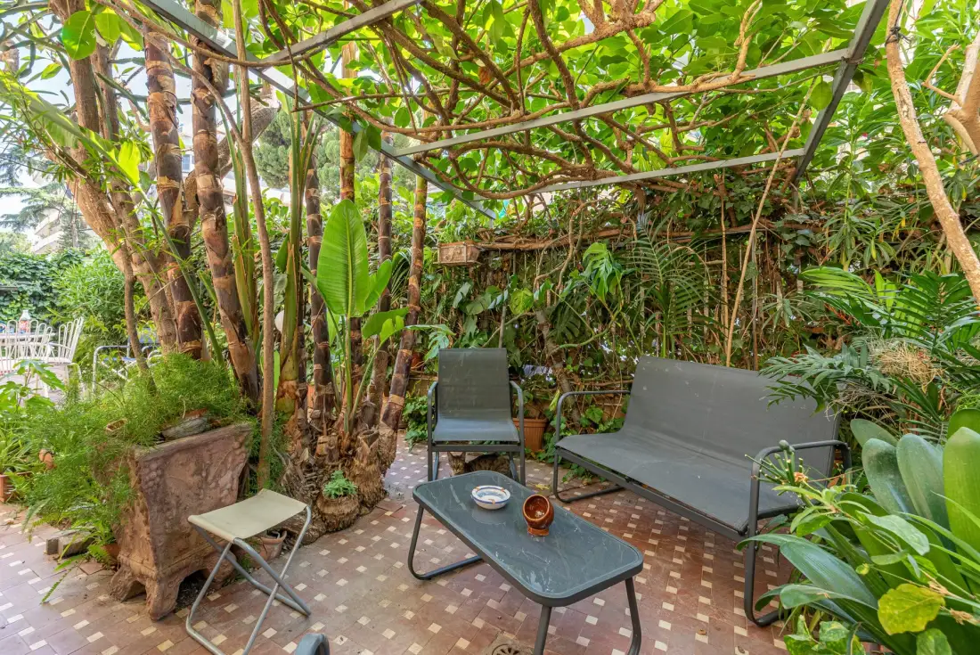 Un patio ajardinado con asientos al aire libre y una mesa baja bajo una pérgola cubierta de enredaderas.
