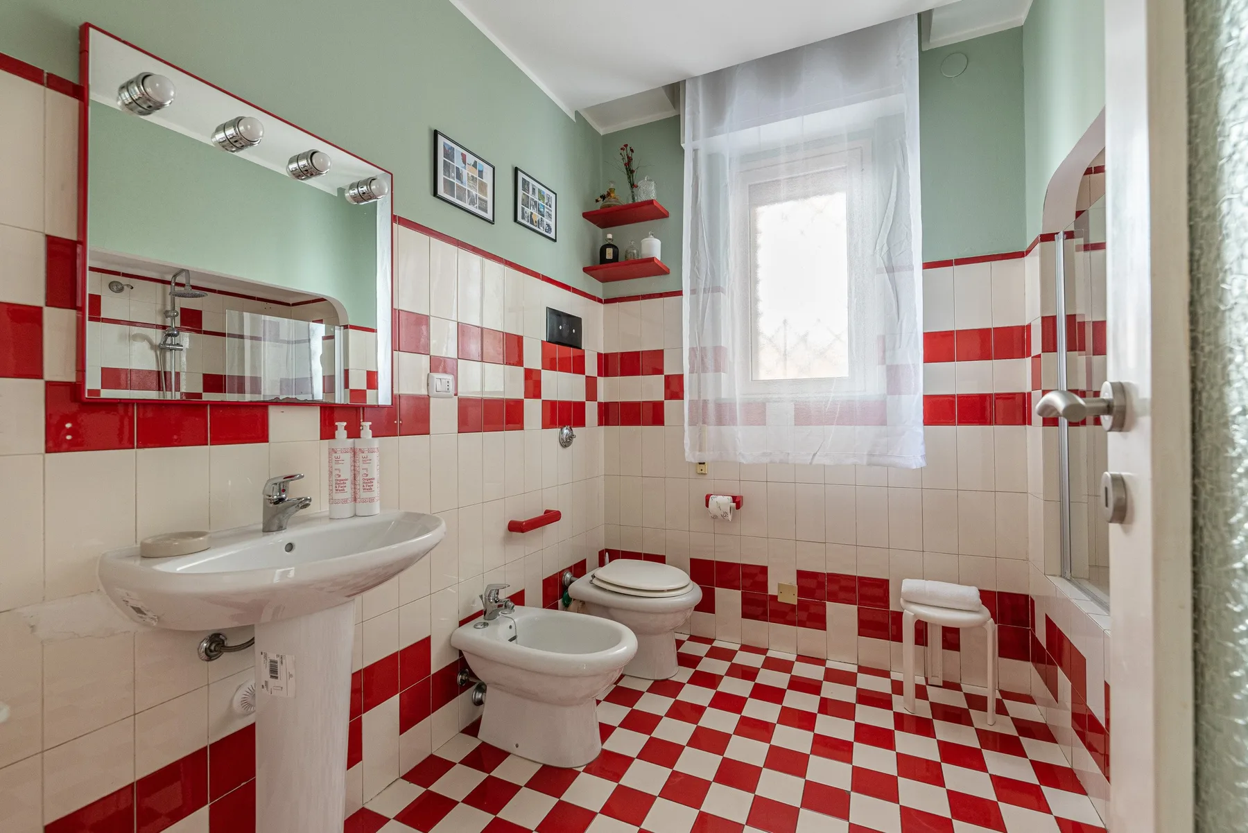 Un baño con lavabo de pedestal, inodoro, bidé y superficies de azulejos rojos y blancos.