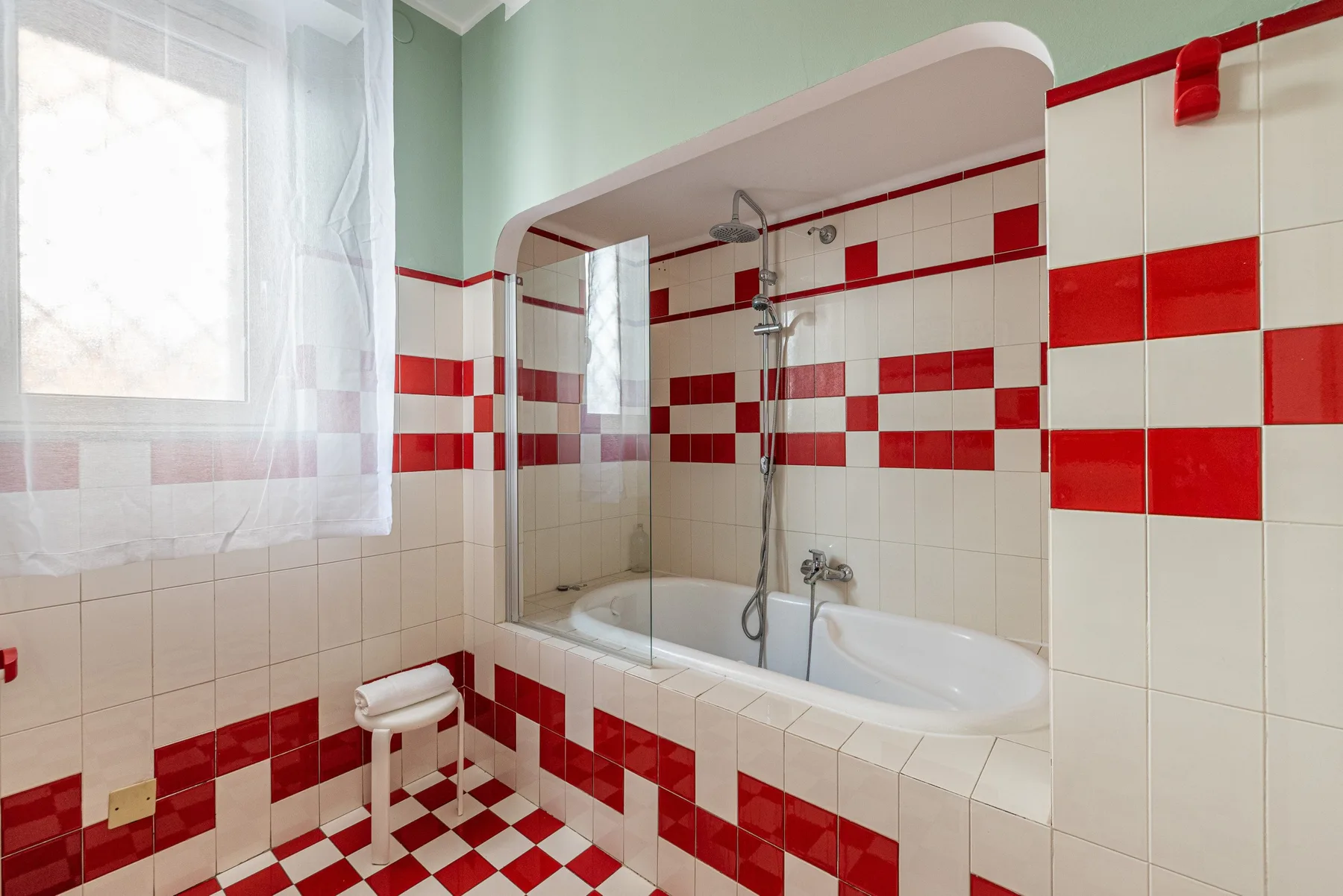 Un baño con bañera, ducha y paredes de azulejos rojos y blancos.
