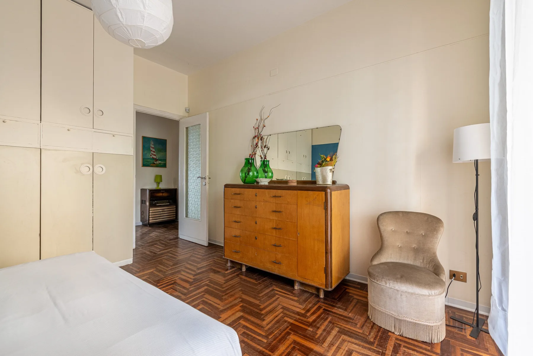 Un dormitorio con una cómoda de madera, un asiento tapizado y suelo de parquet estampado.