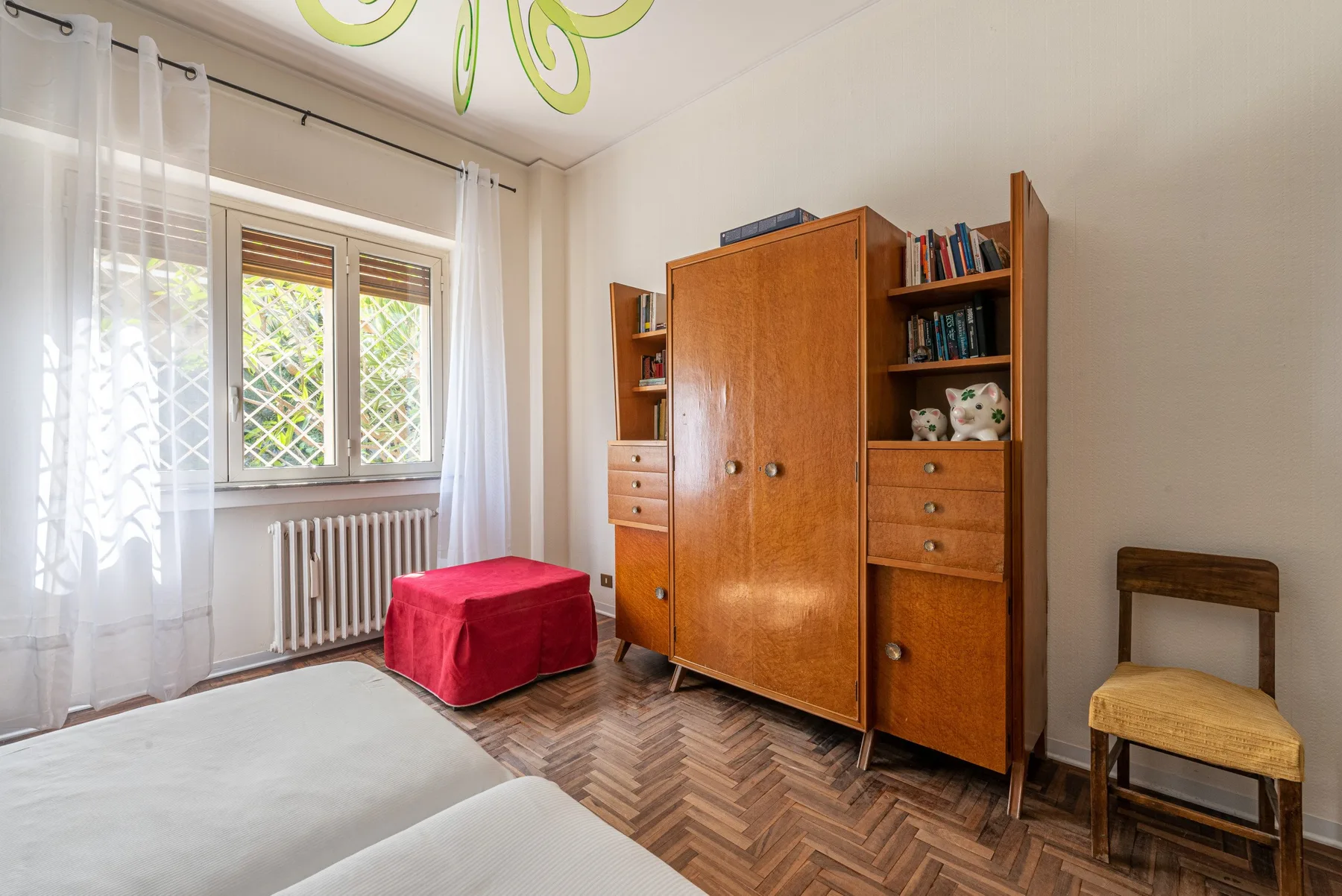 Un dormitorio con muebles de almacenamiento de madera, una ventana y un asiento tapizado rojo.