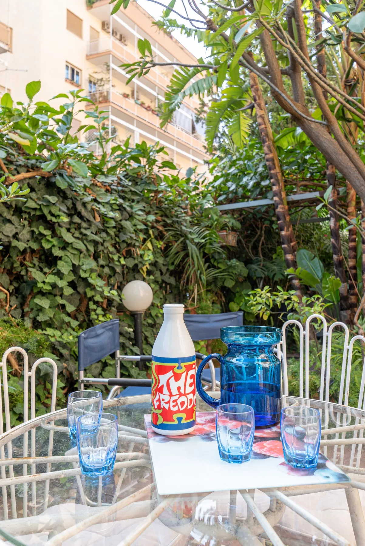 Un patio ajardinado con una mesa de vidrio y vasos de colores.