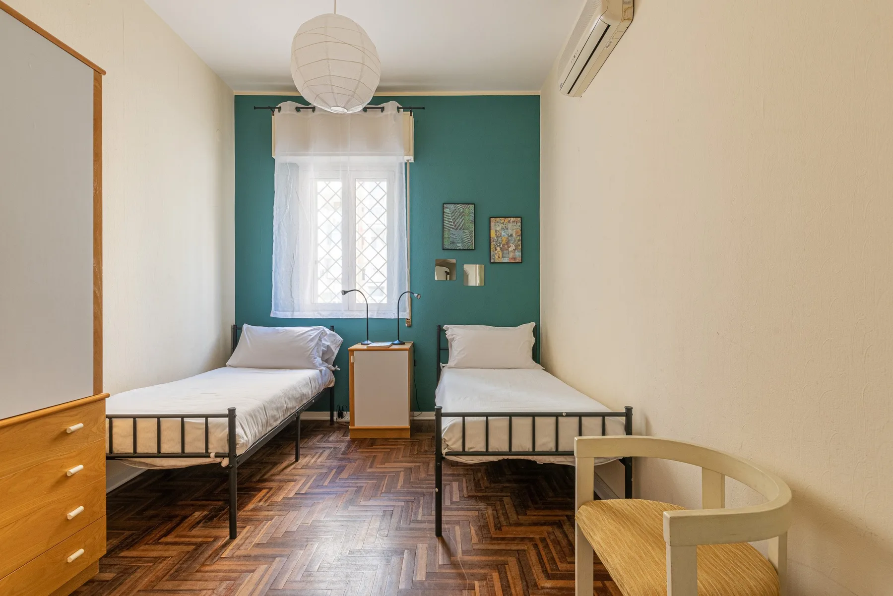 Un dormitorio con dos camas, una pared de acento verde azulado y una mesita de noche.