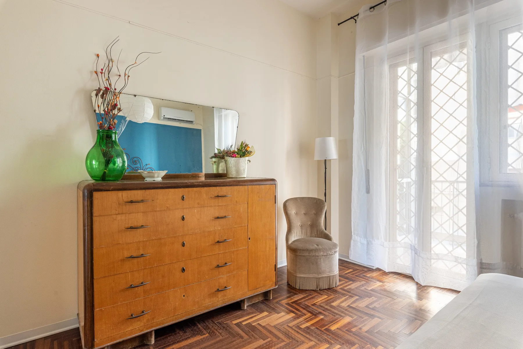 Una habitación luminosa con una cómoda de madera, asientos y cortinas translúcidas junto a las ventanas.