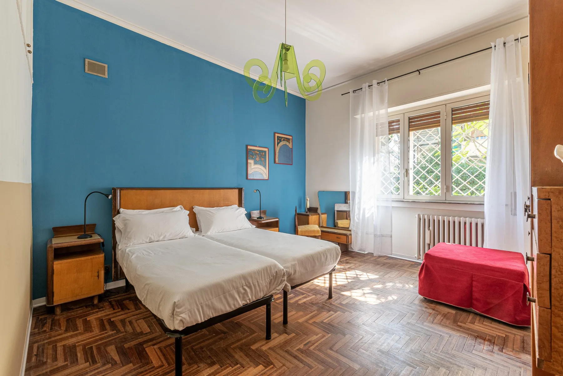 Un dormitorio con una cama, una pared azul y ventanas iluminadas por el sol.