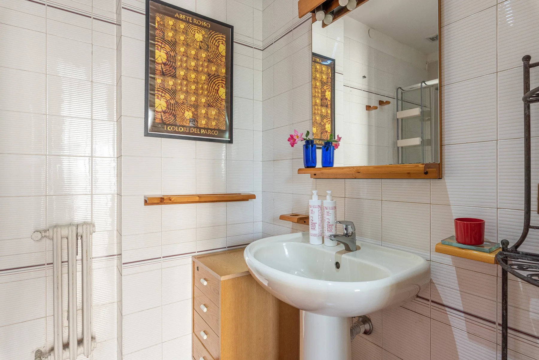 Un baño alicatado con lavabo, espejo y radiador de pared.