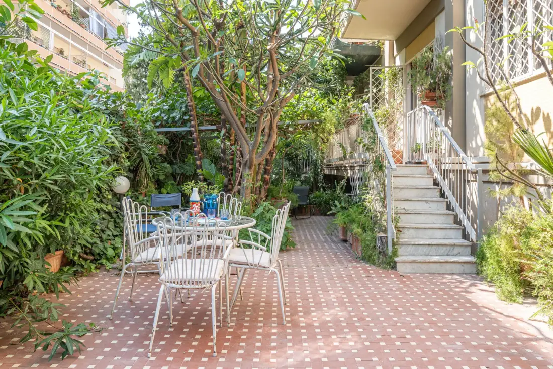 Un patio exterior frondoso con una mesa y asientos junto a una escalera.