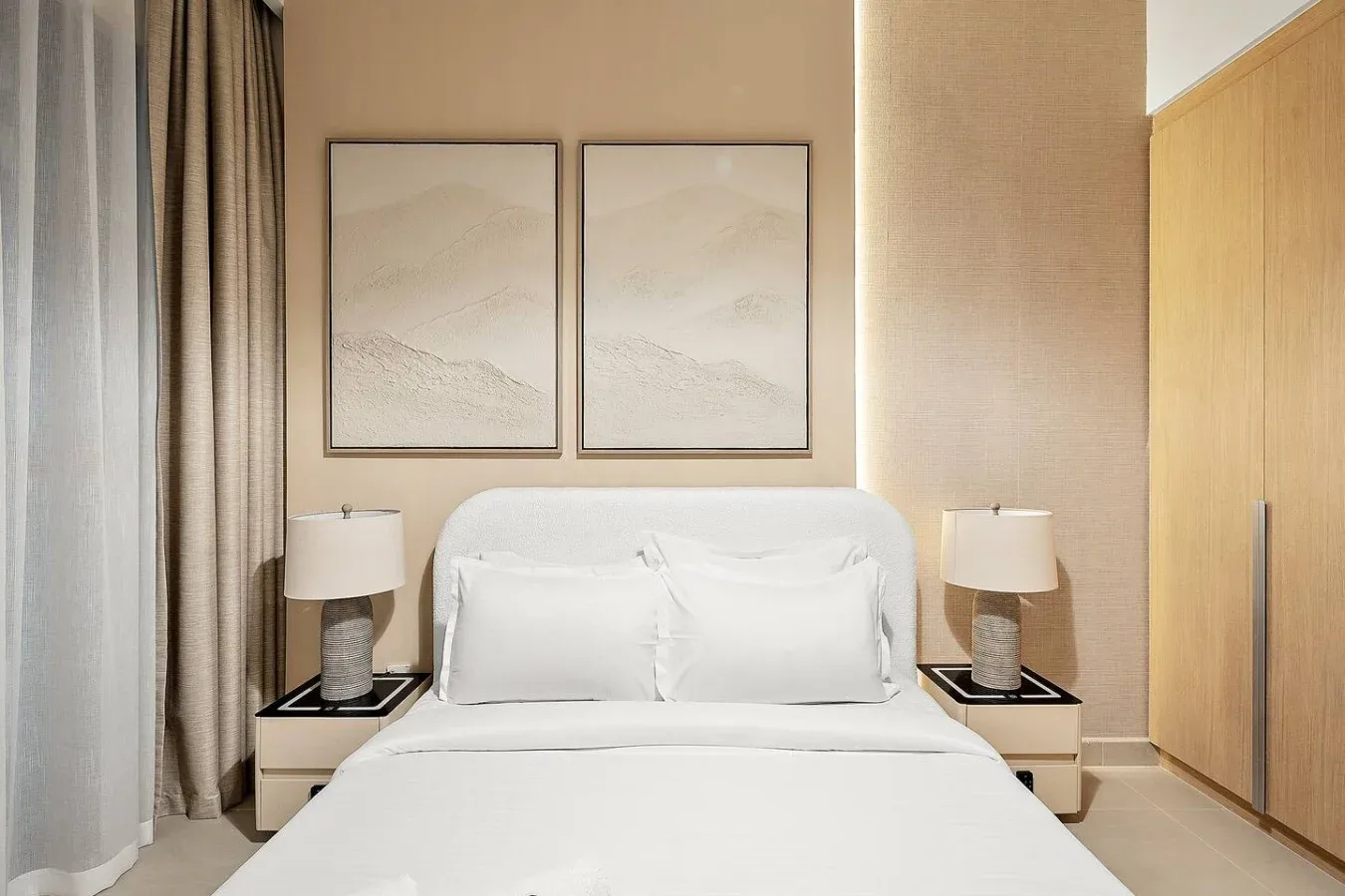 A bedroom with a neatly made bed, matching bedside tables, and framed wall art.