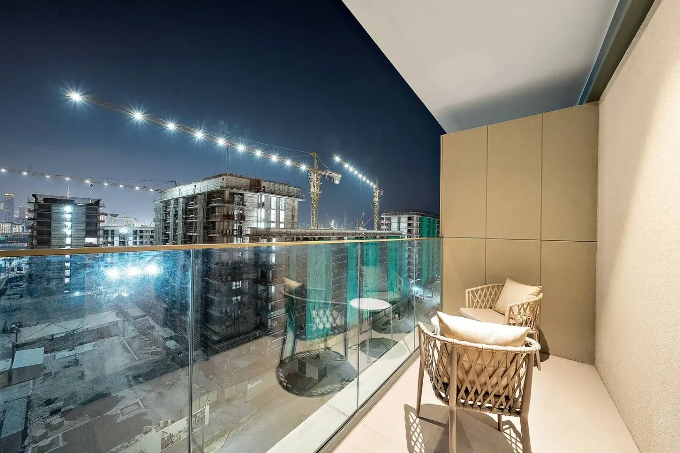 A balcony with seating overlooks illuminated buildings and construction at night.