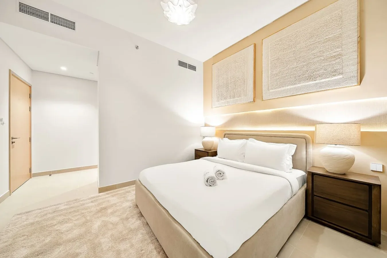 A bright bedroom with a neatly made bed and framed wall art.