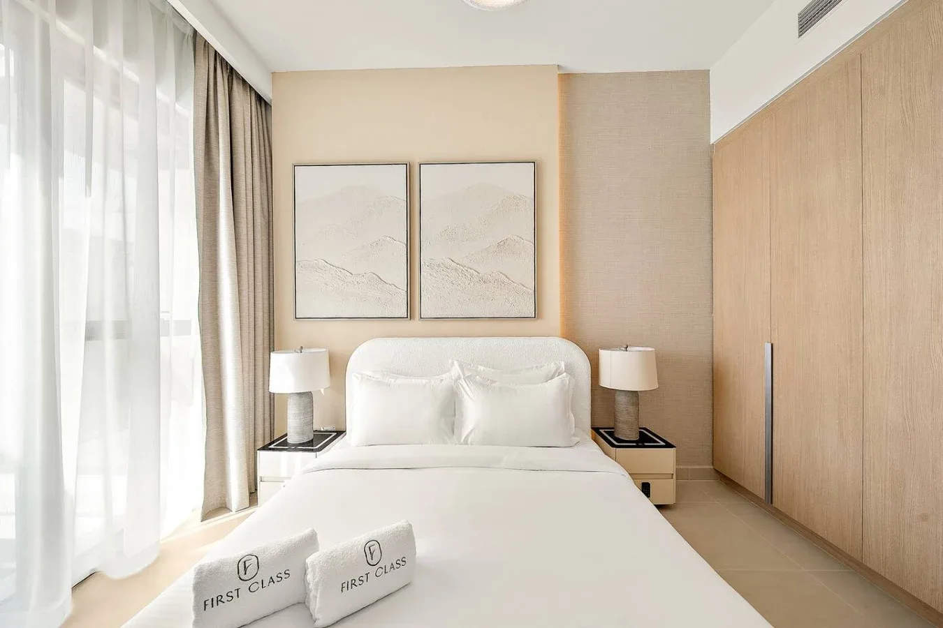 A bright bedroom with a neatly made bed and framed artwork above it.