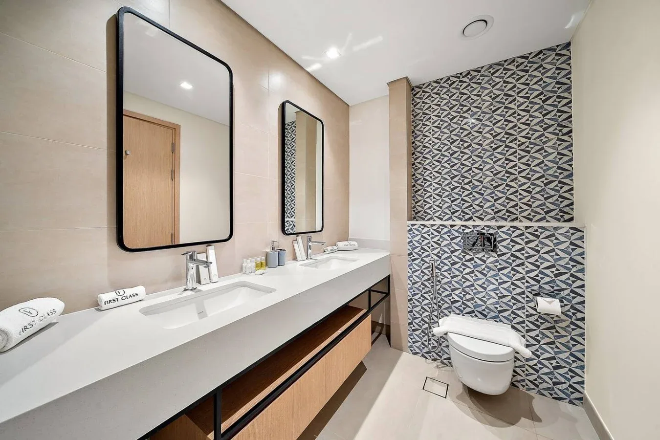 A bathroom with a long vanity, wall mirrors, and a toilet against patterned tile.