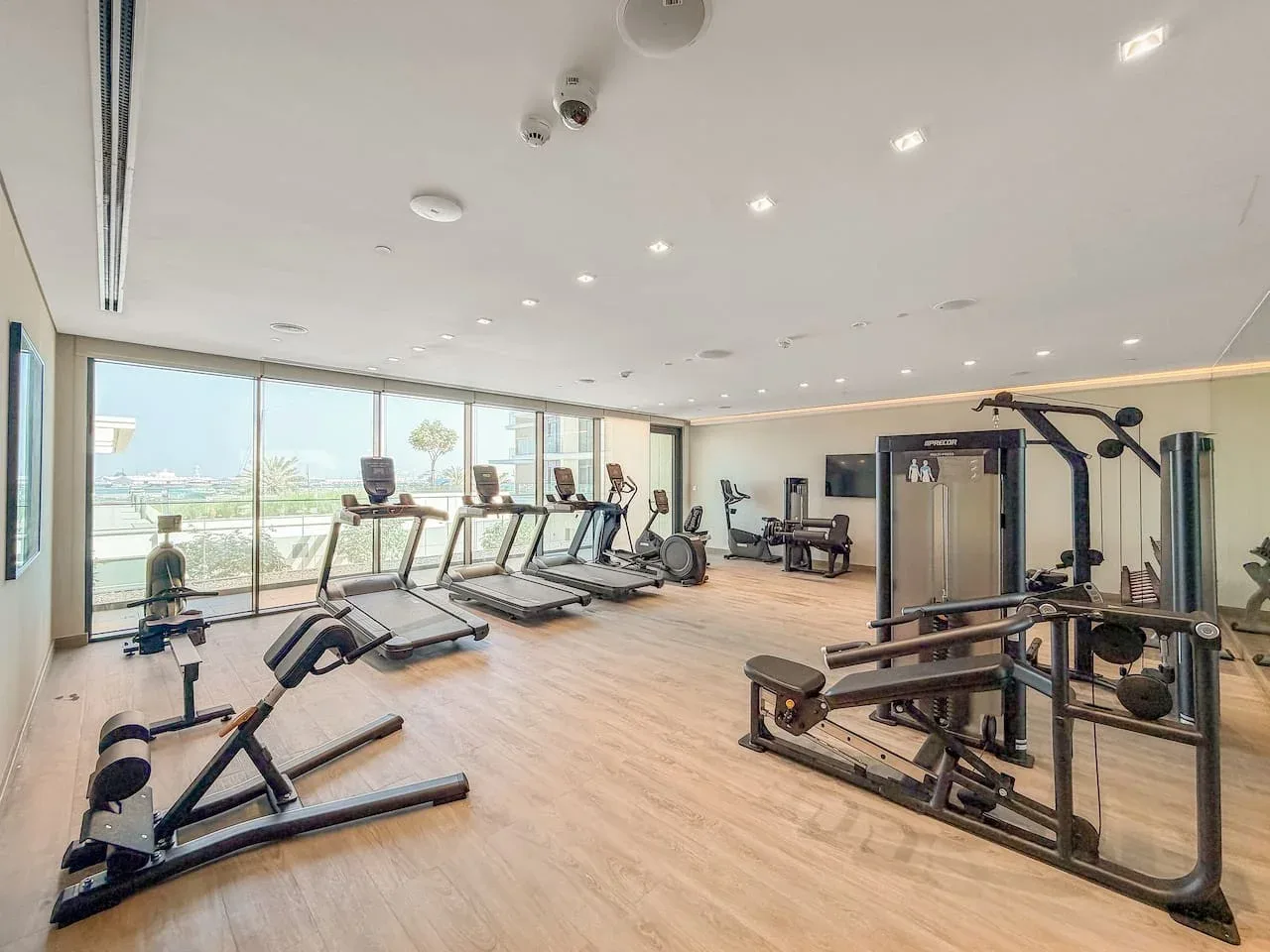 A fitness room with exercise machines and large windows.