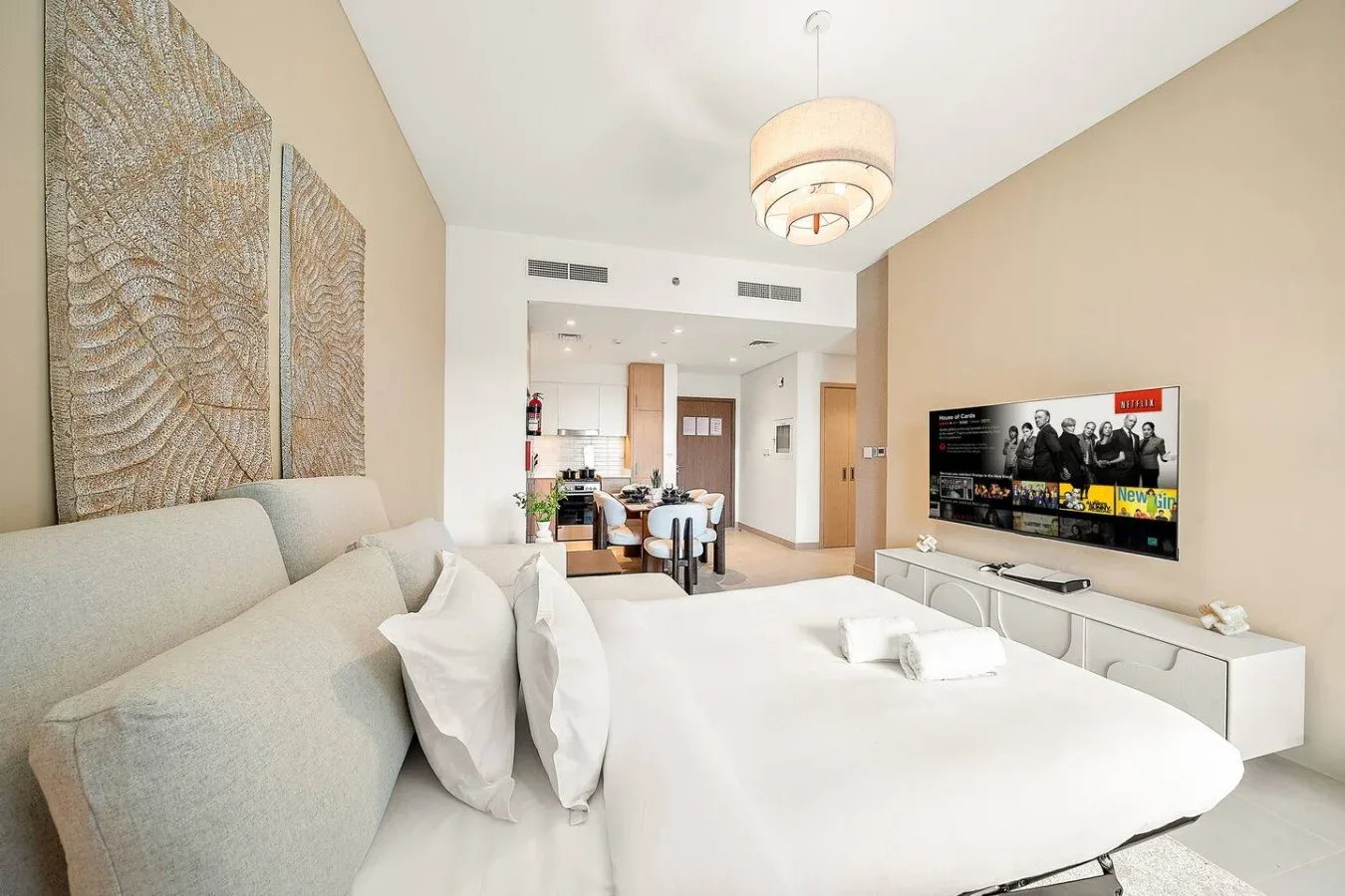 A bright bedroom with a large bed and a dining area visible beyond it.