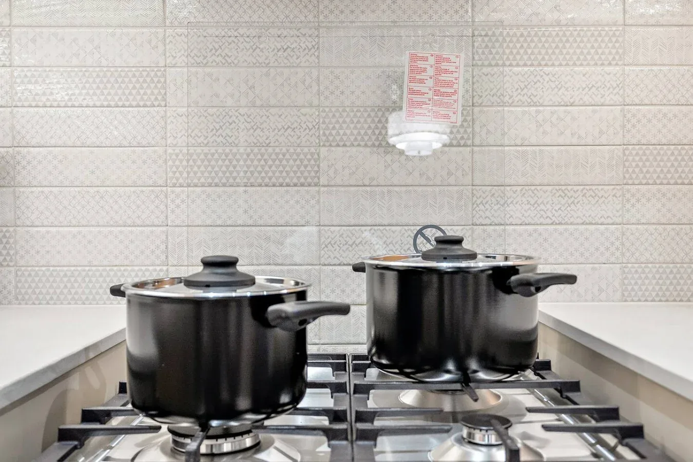A kitchen stovetop with two pots beneath a tiled backsplash.