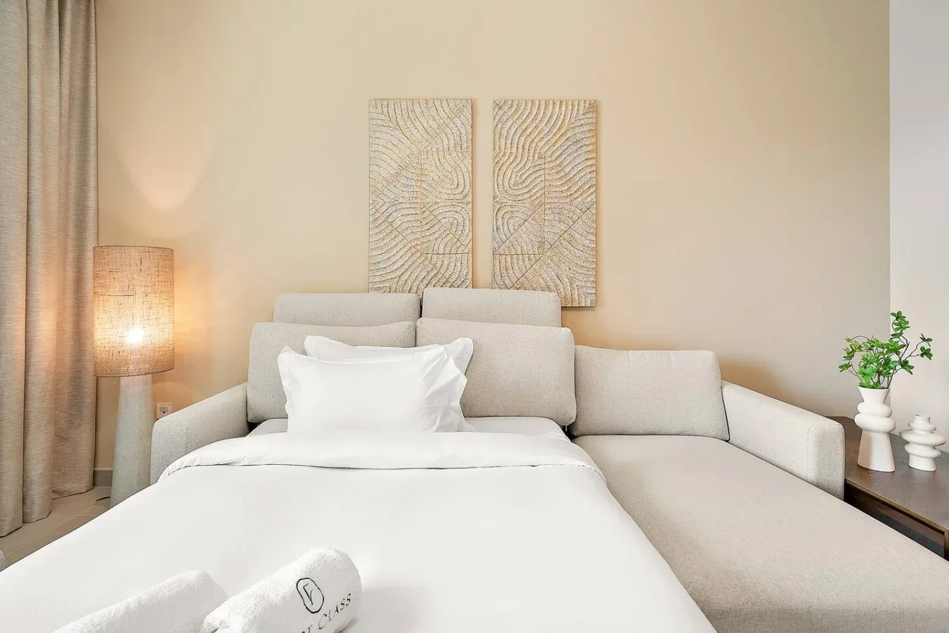 A bedroom with a neatly made bed and a light-colored seating area.