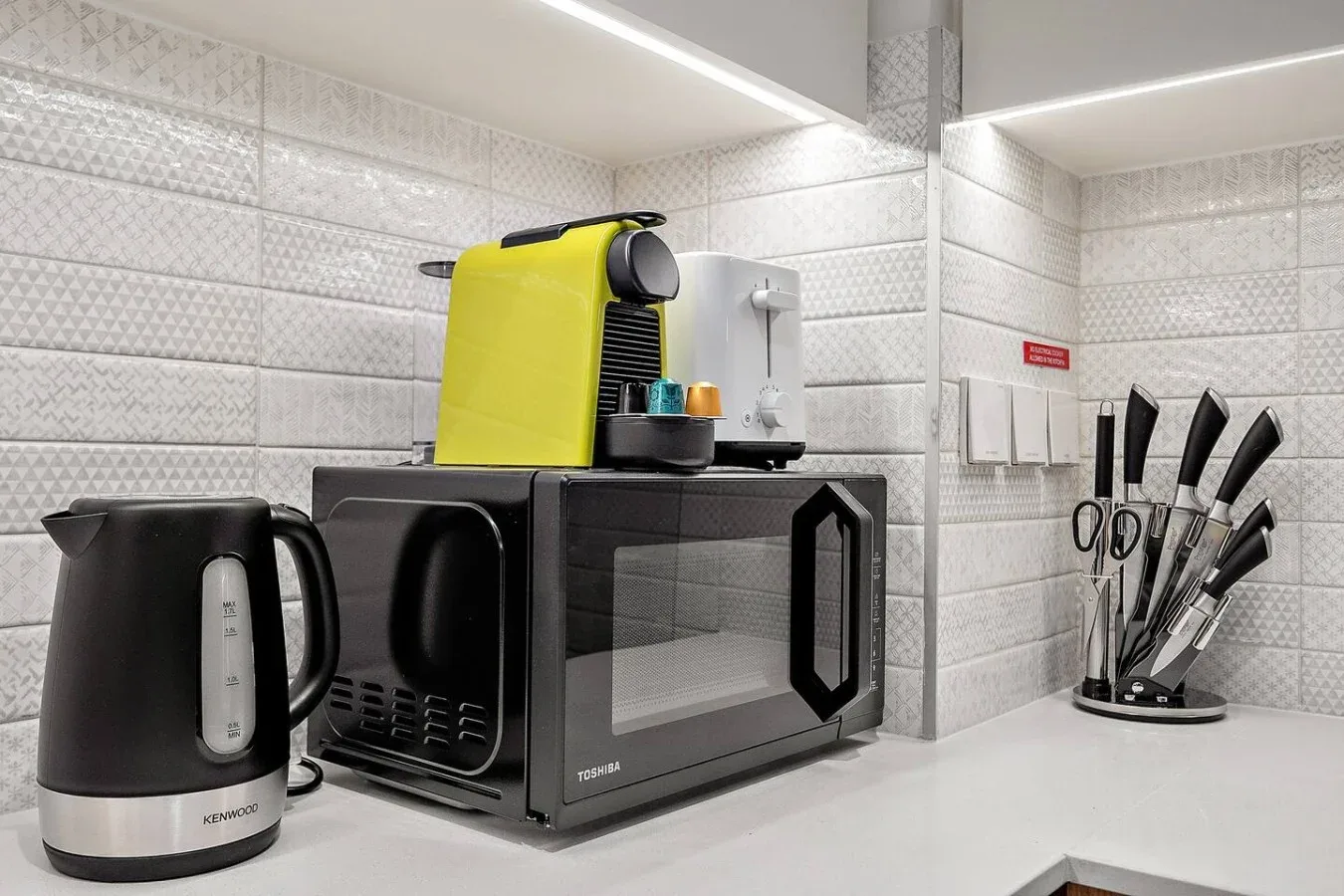 A tiled kitchen counter with a kettle, coffee machine, microwave, and knife block.