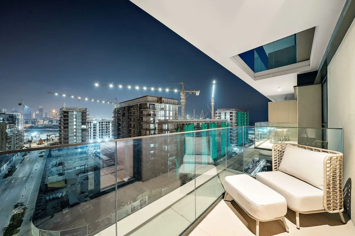 A balcony with cushioned seating overlooks a city construction site at night.