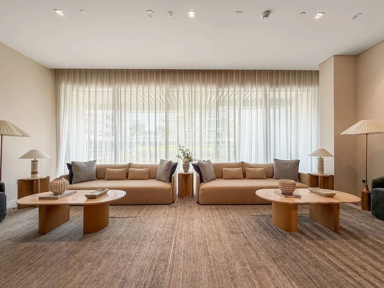 A bright living room with seating arranged in front of a large curtained window.