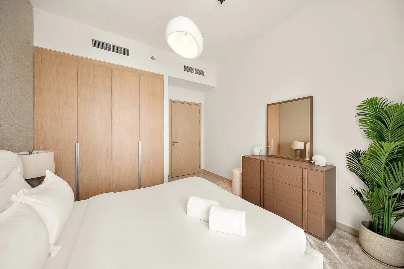 A bright bedroom with a neatly made bed and wooden storage furniture.