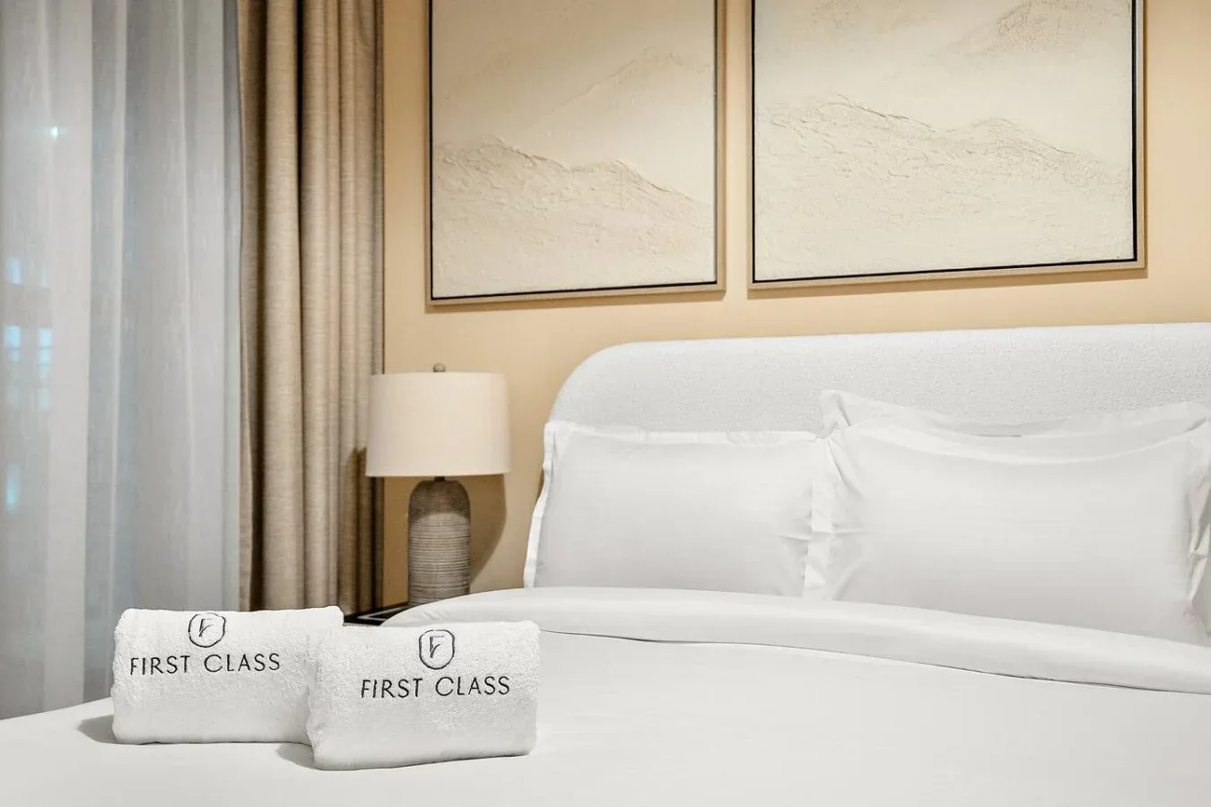 A bedroom with a neatly made bed, framed artwork, and folded towels.