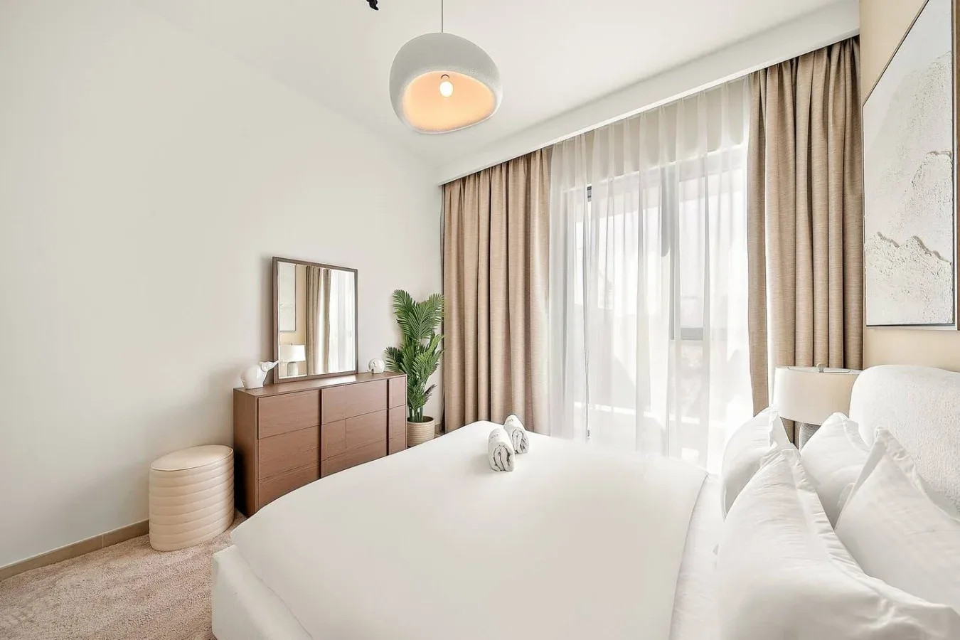 A bright bedroom with a white bed, bedside pillows, and full-length curtains.