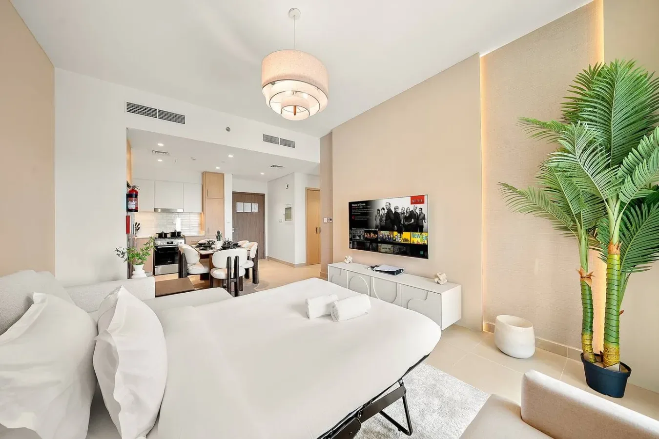 A bright bedroom with a large bed, television, and an open kitchen area.