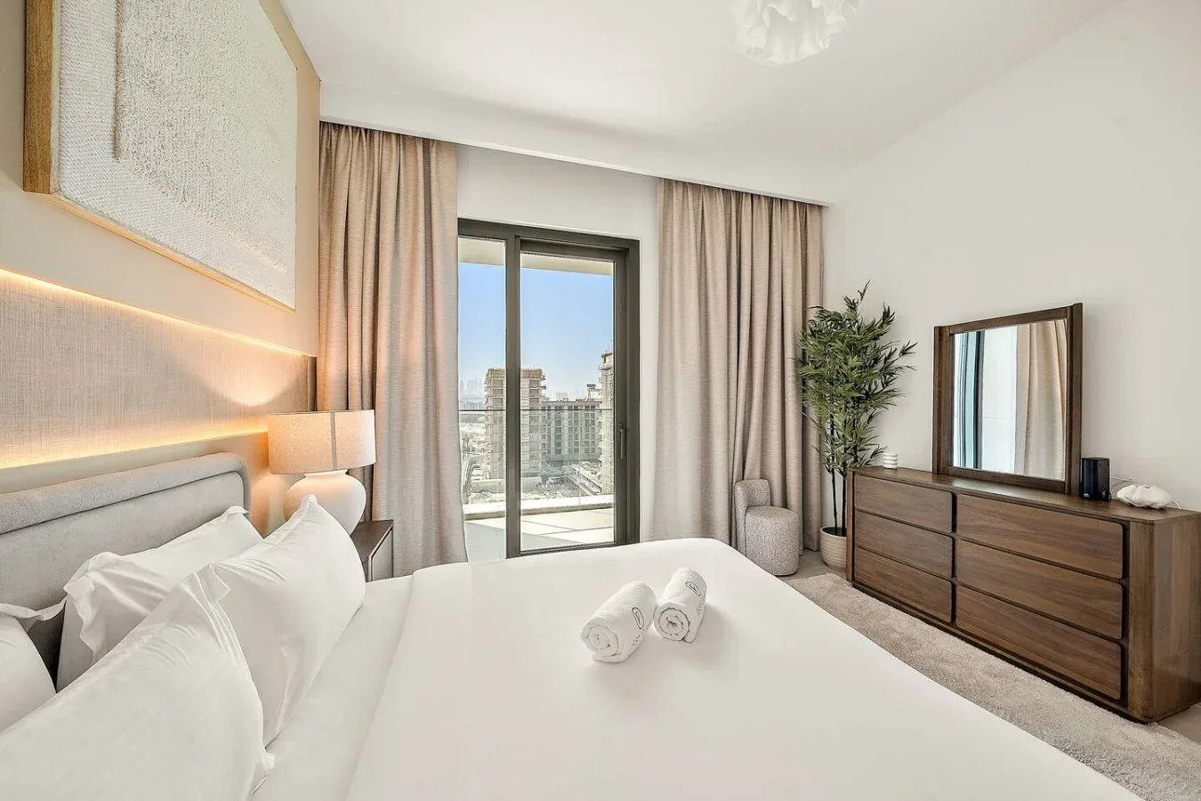 A bright bedroom with a neatly made bed and a glass balcony door.