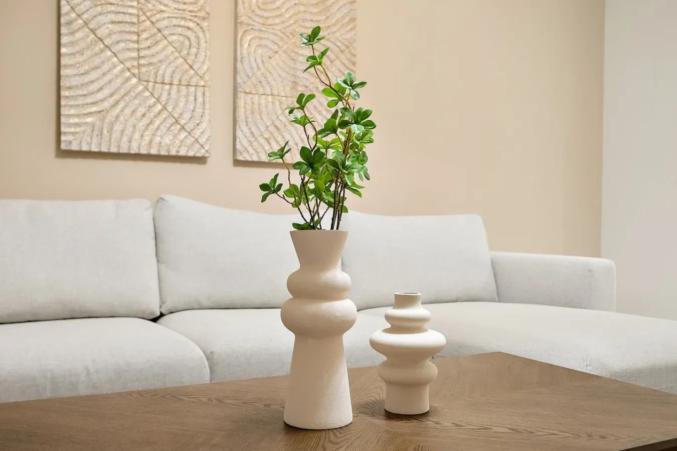 A bright living room features a light-colored sectional and a wooden coffee table with decorative vases.