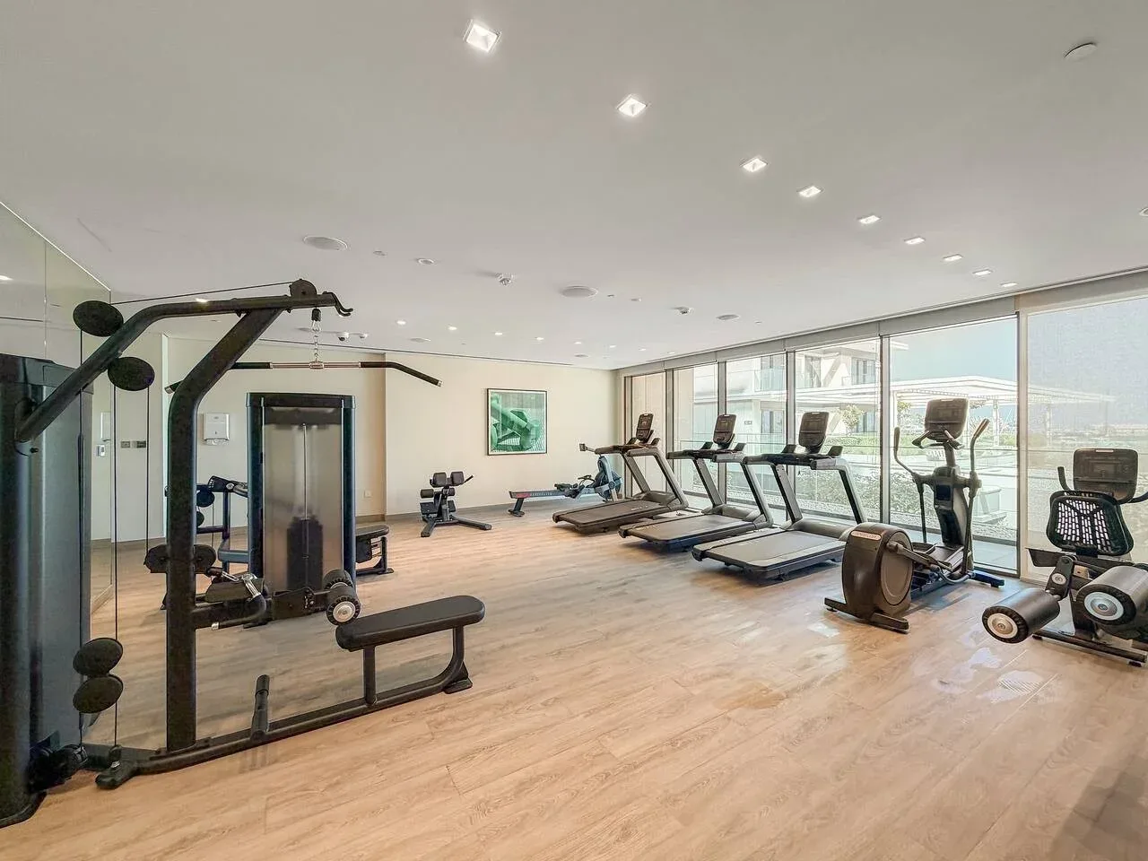 A spacious fitness room has exercise machines, weights, and large windows.
