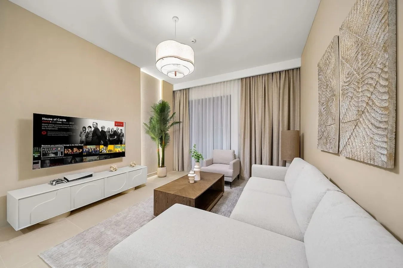 A bright living room with white seating, a low wooden table, and a wall-mounted television.
